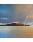 Evening rainbow arcing over a remote Scottish island, with soft light on land and sea.