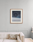 Framed art print of "A Cold Beauty, Lunar Halo" by Nicholas Jones, shown in an elegant, minimalist room with a classic sofa and a window seat. Displayed here in size large.