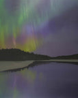 The aurora borealis shimmers above dark trees and a Finnish lake, its colours reflected in the still water.