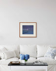 Framed art print of "Aurora Borealis Over Torasieppi" by Nicholas Jones, displayed above a white sofa in a bright, elegant space. A vase of blue hydrangeas sits on the coffee table. Shown here in size medium.