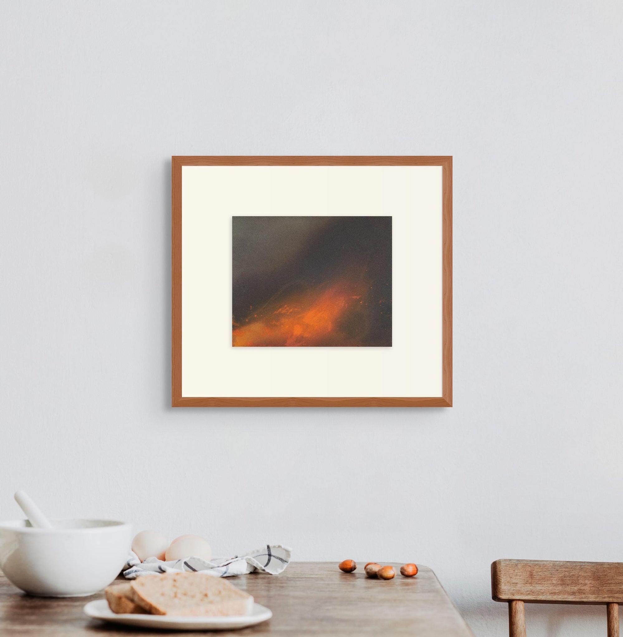 Framed artwork “The fire inside” displayed above a pared-back kitchen setting with a single chair, crockery, and bread.