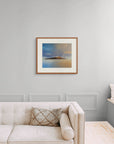 Framed art print of "A Deeper Meeting, Autumn Rainbow Over Holy Isle" by Nicholas Jones, shown in an elegant, minimalist room with a classic sofa and a window seat. Displayed here in size large.