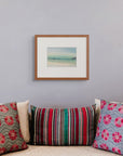Framed art print of "Arctic Coast", displayed above a group of colourful patterned silk cushions set against a pale grey wall.