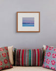 Framed art print of "Dawn, Ilulissat", displayed above a group of colourful patterned silk cushions set against a pale grey wall.