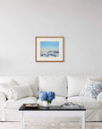 Framed art print of "Fog Bow and Melt Pools" by Nicholas Jones, displayed above a white sofa in a bright, elegant space. A vase of blue hydrangeas sits on the coffee table. Shown here in the size medium.