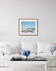 Framed art print of "Fog Bow and Melt Pools" by Nicholas Jones, displayed above a white sofa in a bright, elegant space. A vase of blue hydrangeas sits on the coffee table. Shown here in the size large.