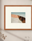 Close-up of the framed fine art print “Heaven and Earth”, hanging on a pale wall, with soft light slanting across it and shadows cast by the delicate branches of dried flowers.
