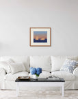 Framed art print of "Icebergs and Moon" by Nicholas Jones, displayed above a white sofa in a bright, elegant space. A vase of blue hydrangeas sits on the coffee table. Shown here in the size medium.