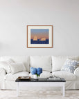 Framed art print of "Icebergs and Moon" by Nicholas Jones, displayed above a white sofa in a bright, elegant space. A vase of blue hydrangeas sits on the coffee table. Shown here in the size large.