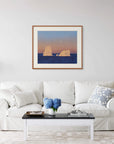 Framed art print of "Icebergs and Moon" by Nicholas Jones, displayed above a white sofa in a bright, elegant space. A vase of blue hydrangeas sits on the coffee table. Shown here in the size extra-large.