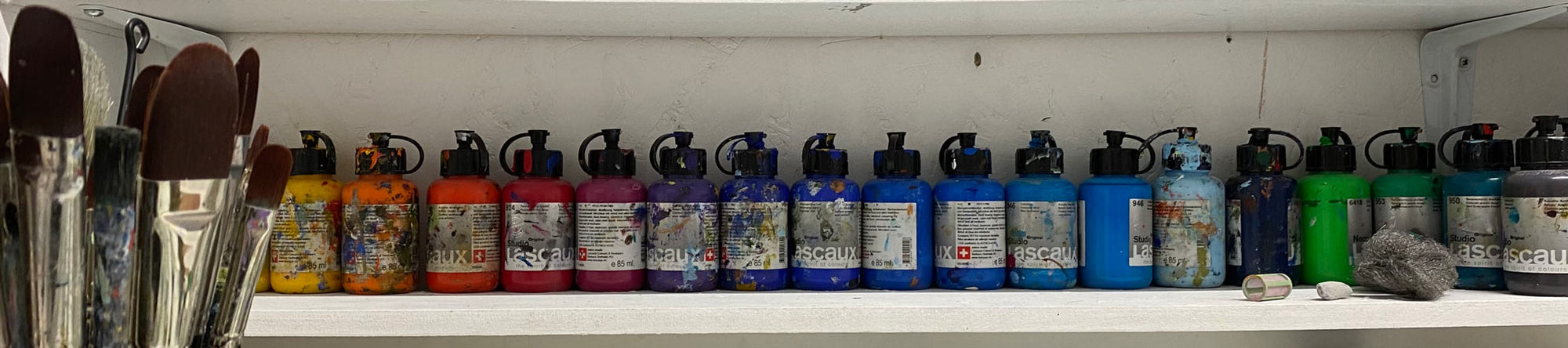 Studio shelf belonging to artist Nicholas Jones, lined with Lascaux acrylic paints and paint brushes — a glimpse behind the scenes.