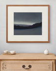 Framed art print of "Luminous Aurora, Forest Edge", displayed above a small wooden chest with three ceramic vessels. A light, quiet space. Shown here in size medium.