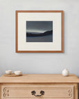Framed art print of "Luminous Aurora, Forest Edge", displayed above a small wooden chest with three ceramic vessels. A light, quiet space. Shown here in size small.