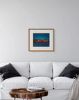 Framed art print of "Mountains and Alpenglow" by Nicholas Jones, shown in a serene pale grey room with a white sofa and soft grey cushions. Displayed here in the size medium.