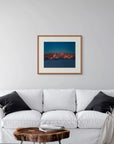 Framed art print of "Mountains and Alpenglow" by Nicholas Jones, shown in a serene pale grey room with a white sofa and soft grey cushions. Displayed here in the size large.