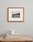 Framed fine art print of “When Flowers Fall" , displayed above a simple rustic wooden bench. Two linen-covered books and a white mug rest quietly on the bench, adding to the calm atmosphere.