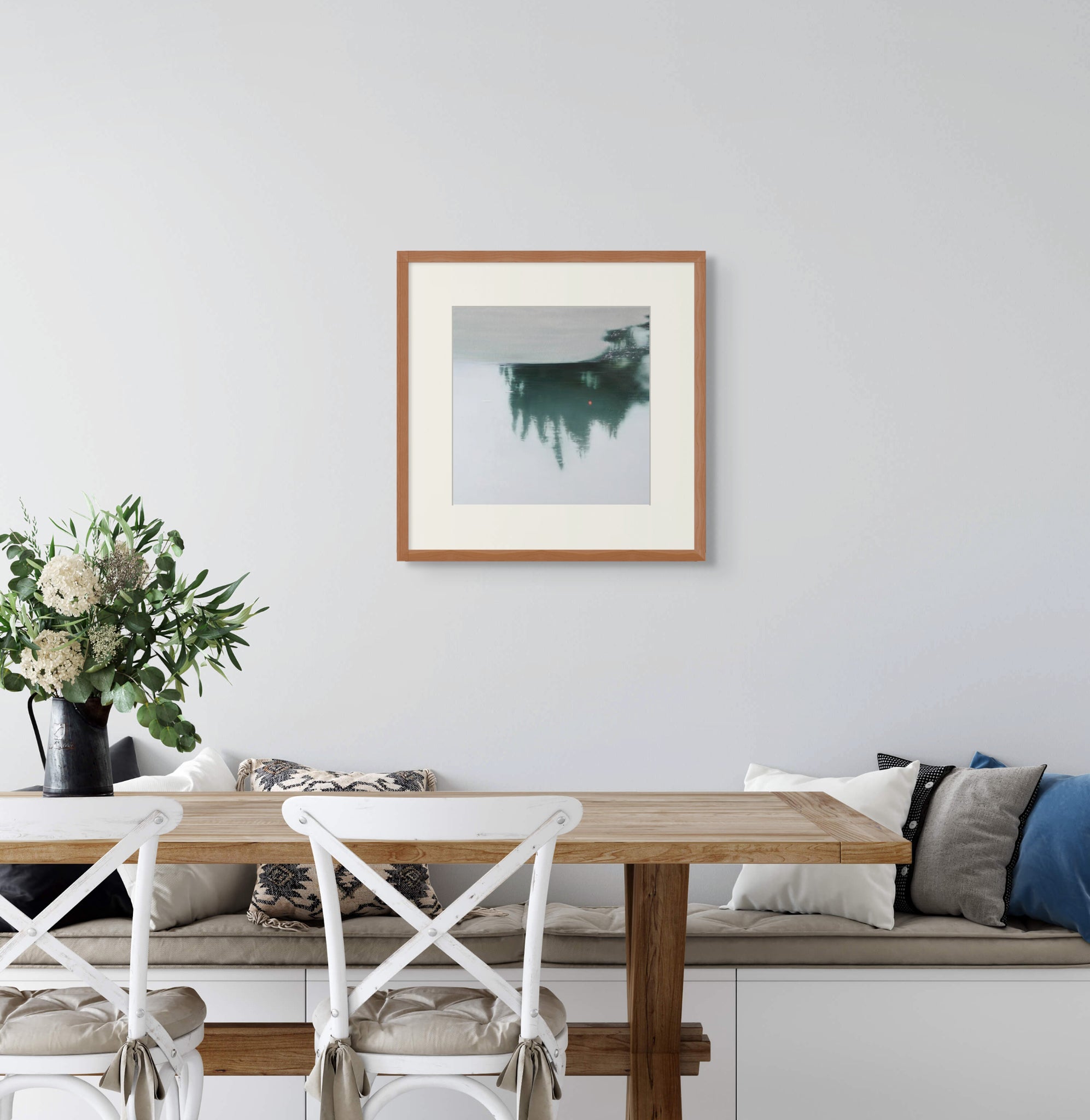 Framed art print of "Beyond the Surface" by Nicholas Jones, shown above a built-in bench in a light-filled kitchen with white chairs and a wooden table set with green and white flowers. Displayed here in size medium.