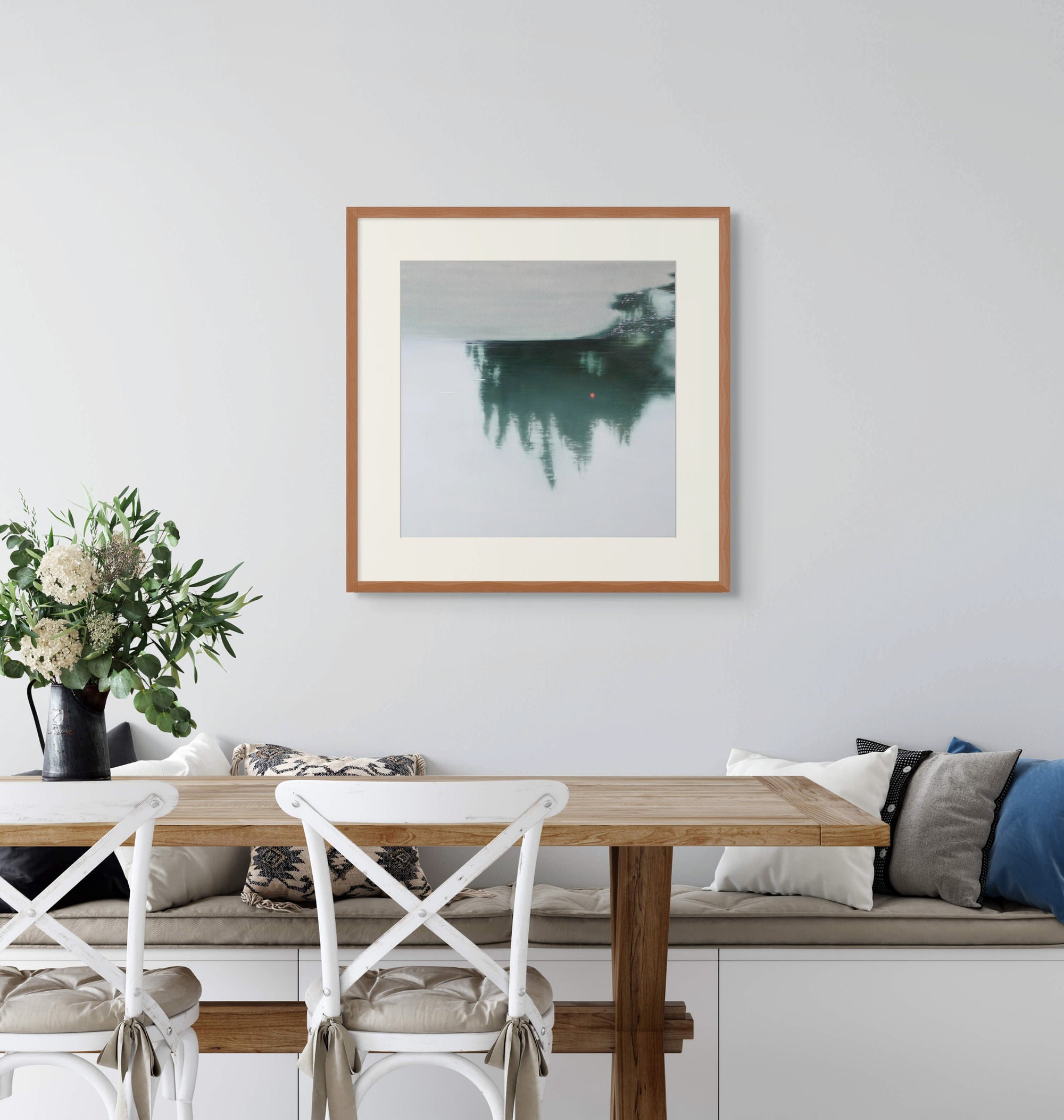 Framed art print of "Beyond the Surface" by Nicholas Jones, shown above a built-in bench in a light-filled kitchen with white chairs and a wooden table set with green and white flowers. Displayed here in size large.